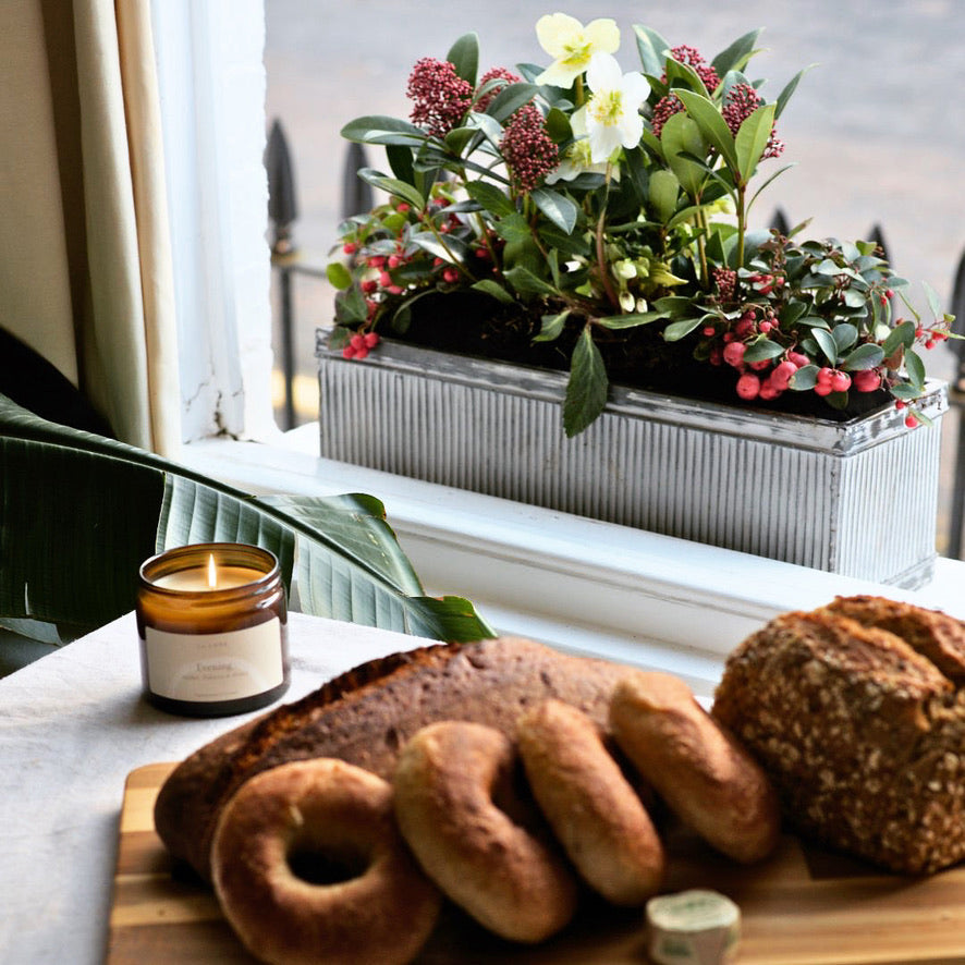 Window box with green, white and red planted flowers with a candle and bagel on the table