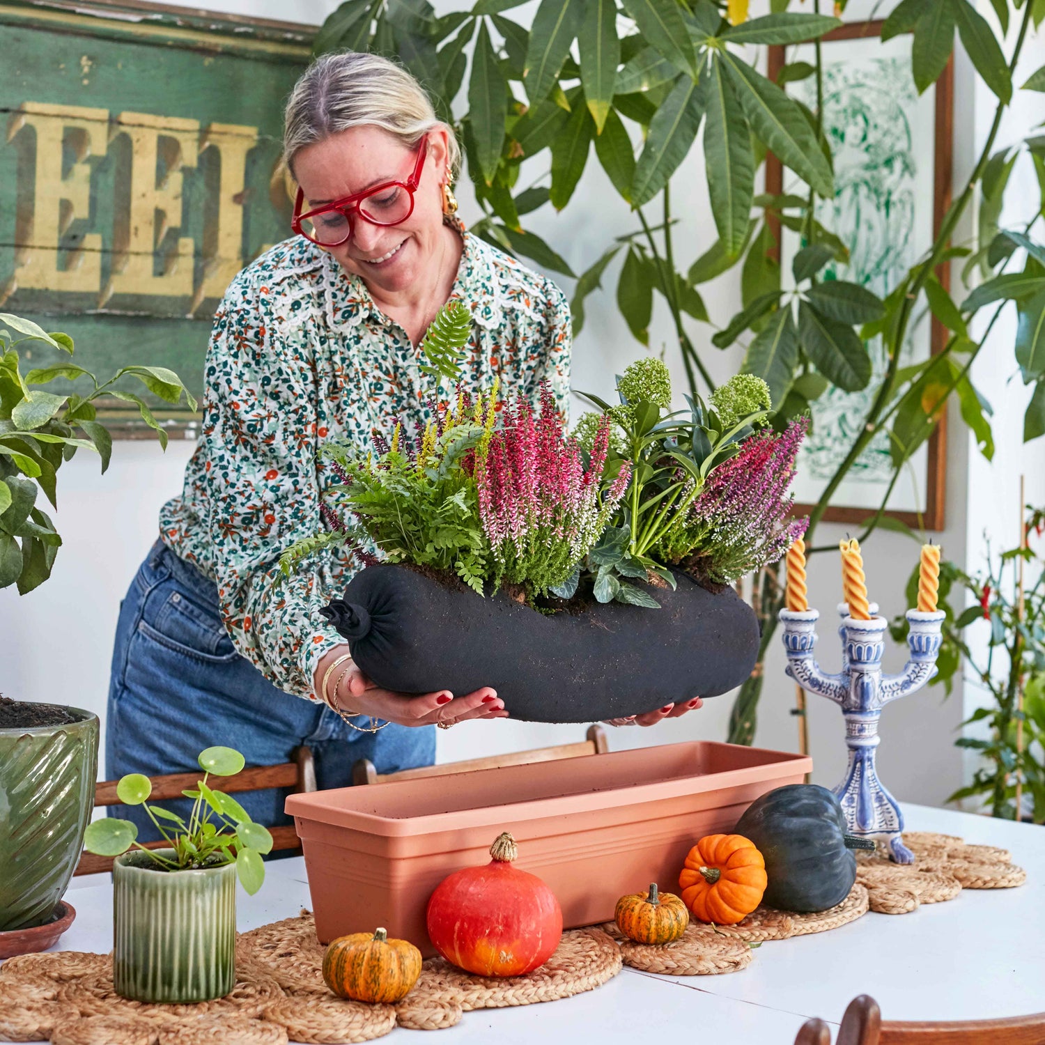 Woman planting flowers in a window box with pumpkins