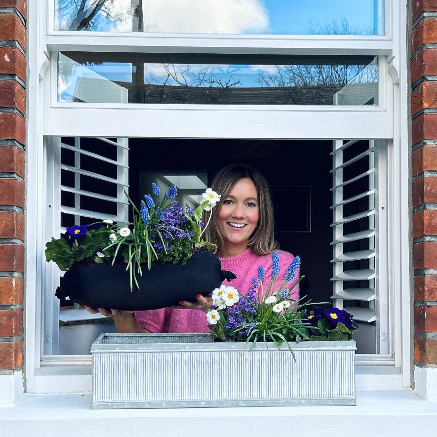 woman placing planted plants into a window box on a window