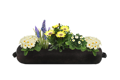 Decorative white, yellow and purple flower arrangement in a black fabric planter insert on a white background